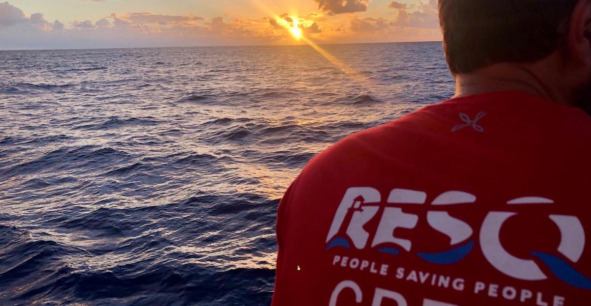 Enrico fotografato da Maso Notarianni. Indossa il giubbotto rosso di ResQ è inquadrato alle spalle e sullo sfondo si vede un bellissimo mare al tramonto